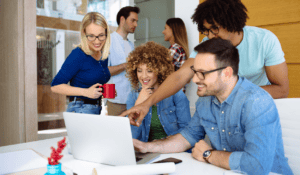 A group of people collaborating as they look at a laptop in an office.