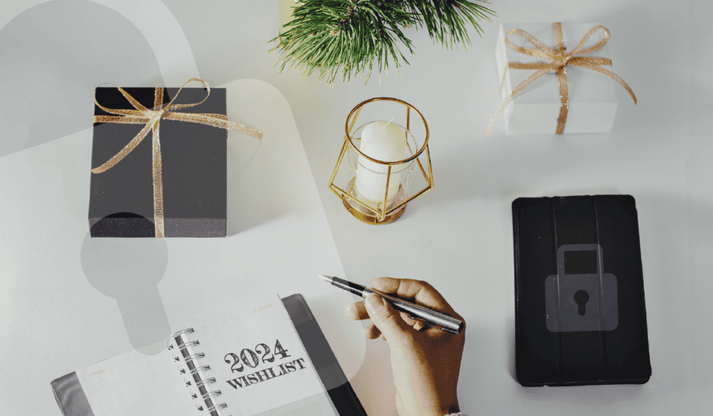Several items on a desk, indicating a secure holiday planning setup: hand holding a pen over a '2024 Wishlist' notebook, a tablet featuring a lock icon on its cover, and elegantly wrapped gifts.