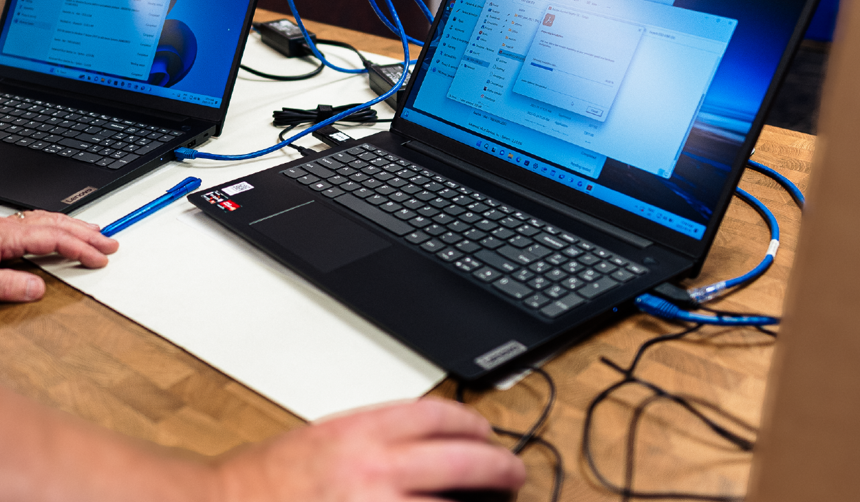 Laptop with connected cables and user navigating file explorer on screen, set on a wooden desk.