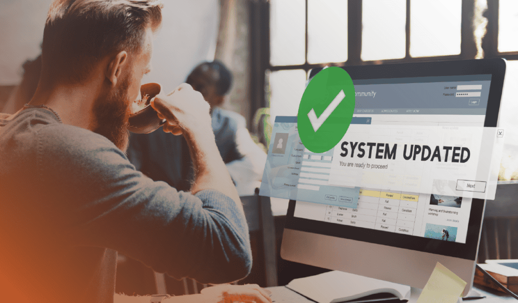 A man who is sipping a cup of coffee is looking at a computer screen. The words "system updated" and a big green checkmark are overlayed on the screen