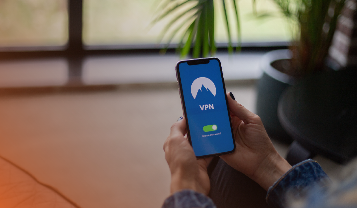 Close-up of a person's hands holding a smartphone displaying a VPN connection screen with the text 'VPN' and an icon indicating 'You are connected' against a blurred indoor background