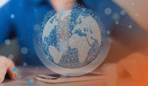 This image represents the topic of the article: "Why Smart IT Solutions for Calgary Businesses Are the Key to Secure, Accessible Information". The image colours are orange and blue. There is a person from the shoulder down, sitting at a desk, wearing a blue shirt. In front of them, is a white cell phone. There is a graphic of a globe overlaid on top of the photo, with lines and nodes representing information and IT.