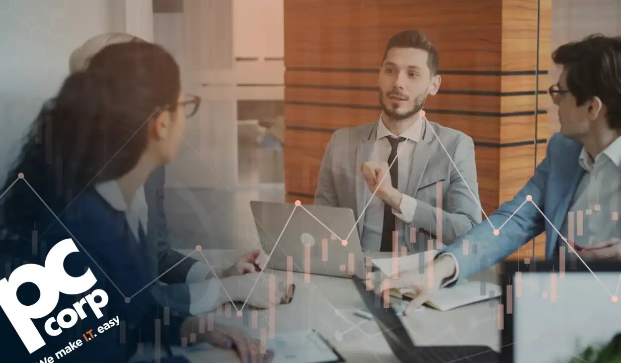The image represents the title and theme of the blog: How to Build a Business Case for an IT Investment That Leadership Will Actually Act On. There is a group of people, men and women, sitting around a conference table, covered in paper.
